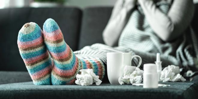 a young woman in comfy socks with a mug, nasal spray, and used tissues