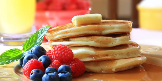 a stack of homemade pancakes from scratch with berries, syrup, and butter