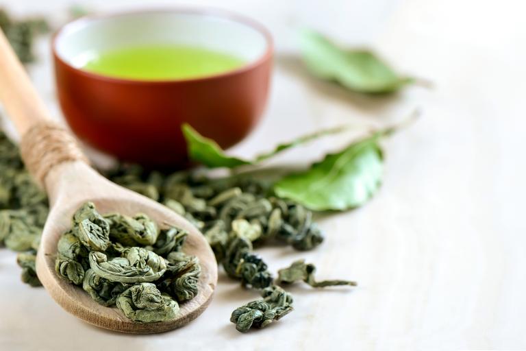 A spoon of dried leaves and a cup of green tea